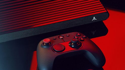 Consola Atari VCS con carcasa de rejilla y mando inalámbrico sobre una superficie oscura bajo iluminación roja.