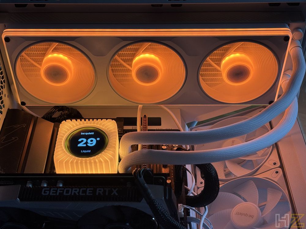 Interior de un ordenador con sistema de refrigeración líquida be quiet! Light Loop instalado, mostrando la pantalla LCD del bloque y tres ventiladores frontales con iluminación naranja.