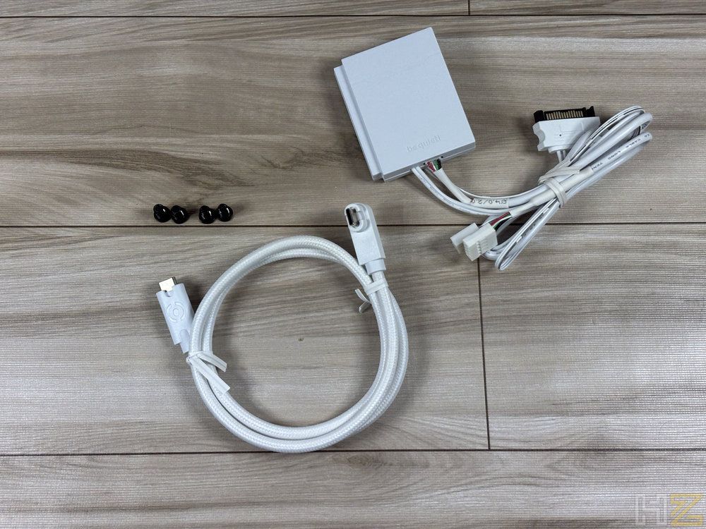 Conjunto de accesorios blancos para ventiladores be quiet! Light Wings Pro, incluyendo un hub ARGB, cableado y tornillos sobre una superficie de madera.