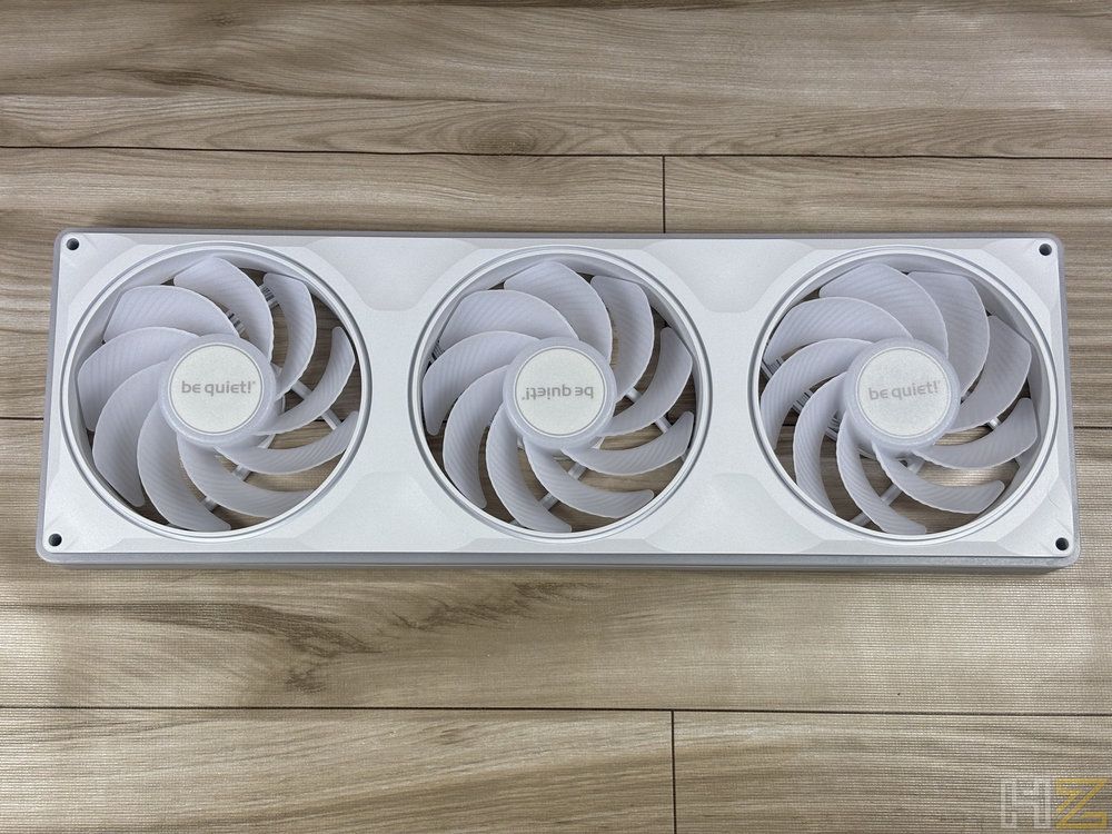 Tres ventiladores blancos be quiet! Light Wings Pro integrados en un marco rectangular sobre una superficie de madera.