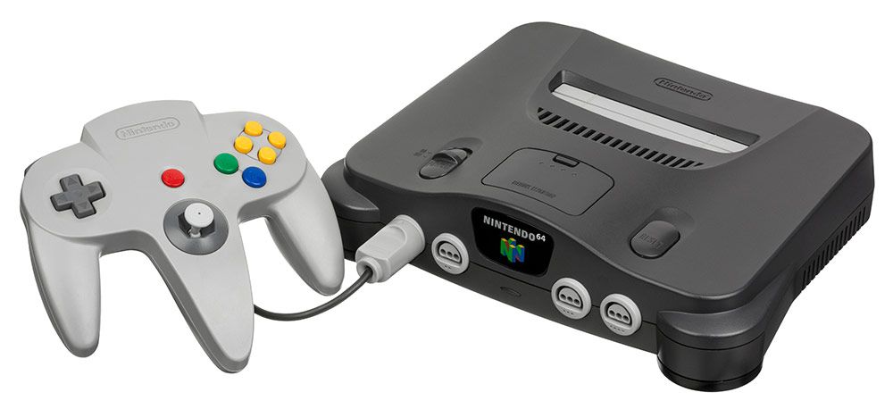 Consola Nintendo 64 de color gris oscuro junto a su mando original de tres agarres en color gris claro.