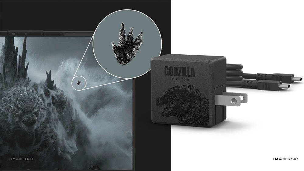 Detalle de una huella de Godzilla en la pantalla de un dispositivo y adaptador de corriente temático de Godzilla Minus One.