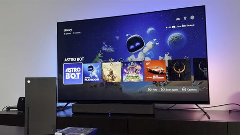 Interfaz de PlayStation 5 en un televisor junto a una consola Xbox Series X