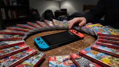 Consola Nintendo Switch rodeada de cajas de juegos en formato físico sobre una mesa de madera.
