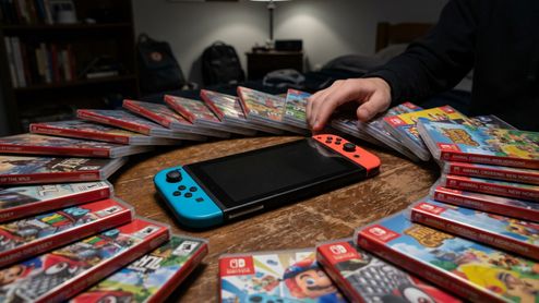 Consola Nintendo Switch rodeada de cajas de juegos en formato físico sobre una mesa de madera.