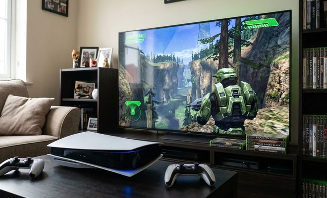 Consola PS5 con mandos DualSense frente a un televisor que muestra una partida del videojuego Halo.