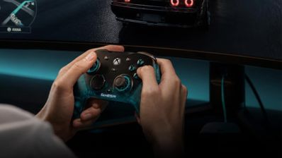 Primer plano de una persona sujetando un mando Gamesir con botones retroiluminados frente a un monitor curvo.