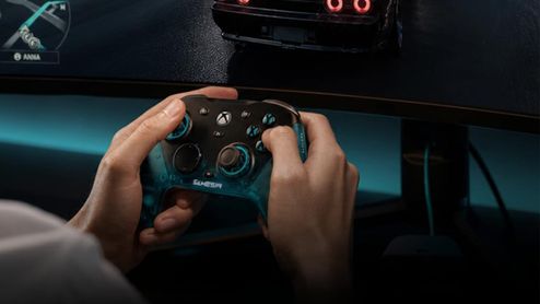 Primer plano de una persona sujetando un mando Gamesir con botones retroiluminados frente a un monitor curvo.