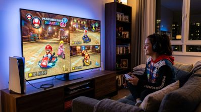 Una persona juega a Mario Kart 8 Deluxe en pantalla dividida sentada frente a un televisor con una consola PS5 al lado.