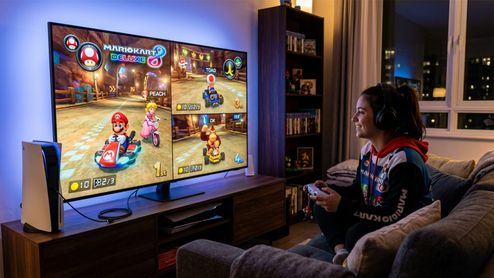 Una persona juega a Mario Kart 8 Deluxe en pantalla dividida sentada frente a un televisor con una consola PS5 al lado.
