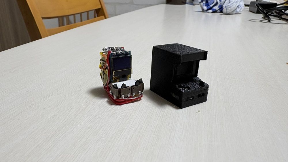 Circuito electrónico ensamblado con pantalla pequeña junto a una carcasa de mini recreativa impresa en negro.