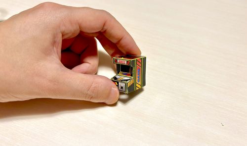 Una mano humana sujetando una réplica minúscula de una máquina recreativa arcade entre los dedos índice y pulgar.