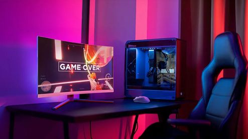 Monitor curvo Philips para videojuegos mostrando pantalla de Game Over junto a una torre de ordenador con iluminación LED azul en una habitación con luz ambiental púrpura.