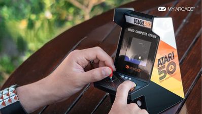 Primer plano de una persona utilizando la consola portátil My Arcade Atari Micro Player Pro sobre una mesa de madera.