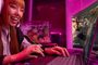 Una mujer joven con auriculares gaming blancos utiliza un ordenador portátil Intel de gama alta en una habitación con iluminación LED rosa.