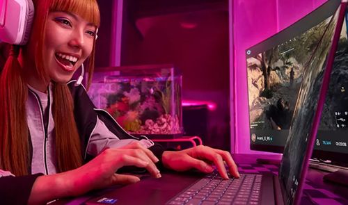 Una mujer joven con auriculares gaming blancos utiliza un ordenador portátil Intel de gama alta en una habitación con iluminación LED rosa.