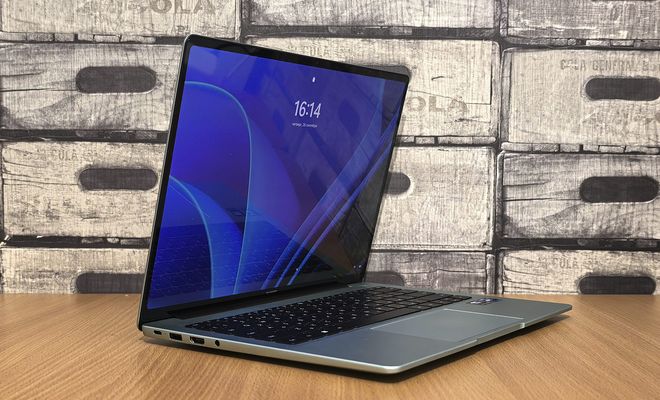 Ordenador portátil abierto sobre una mesa de madera mostrando la pantalla de bloqueo de Windows 11.
