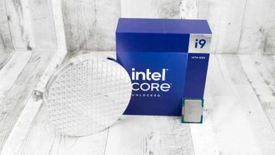 Procesador Intel Core i9-14900 junto a su embalaje azul y una oblea de silicio sobre una superficie de madera clara.
