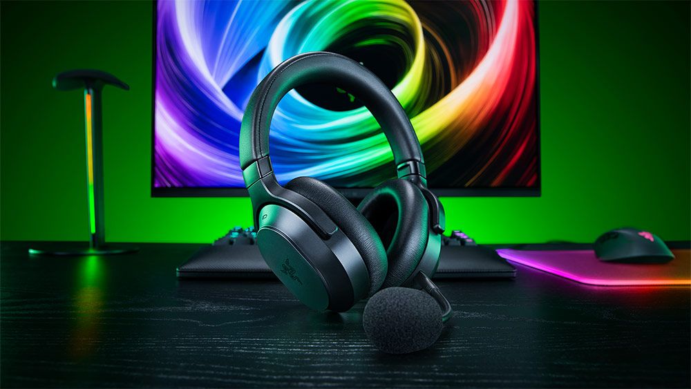 Auriculares Razer Barracuda V2 apoyados en un escritorio frente a un monitor con fondo multicolor.