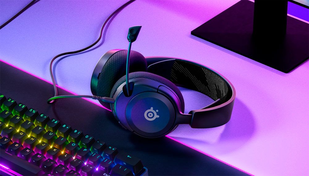 Auriculares SteelSeries Arctis Nova 1 sobre una mesa de escritorio con iluminación ambiental morada y teclado RGB.
